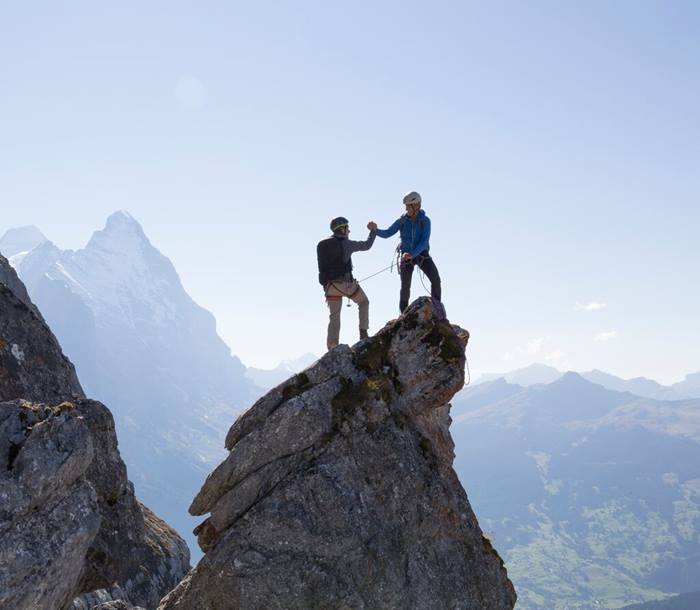 Two climbers exchange handshake on pinnacle summit